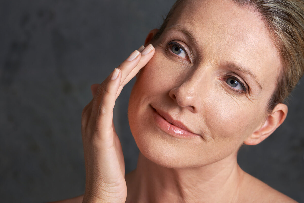 A woman in her fifties touching her cheek, studio light